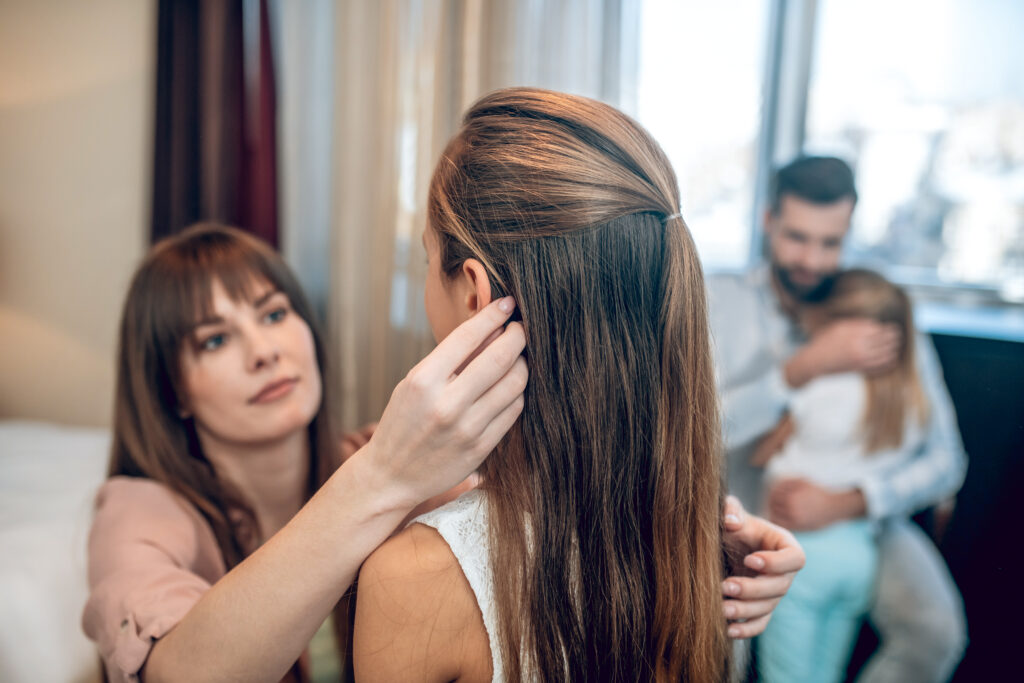 Mother grooming daughters hair with family in the background
