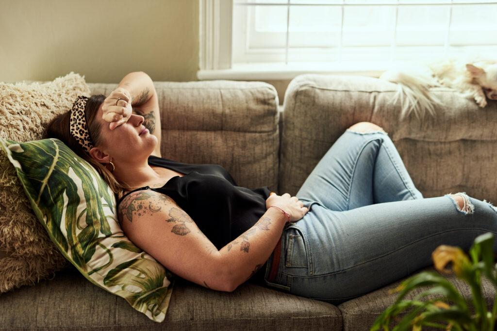 Woman laying on couch in pain with her forearm over her forehead