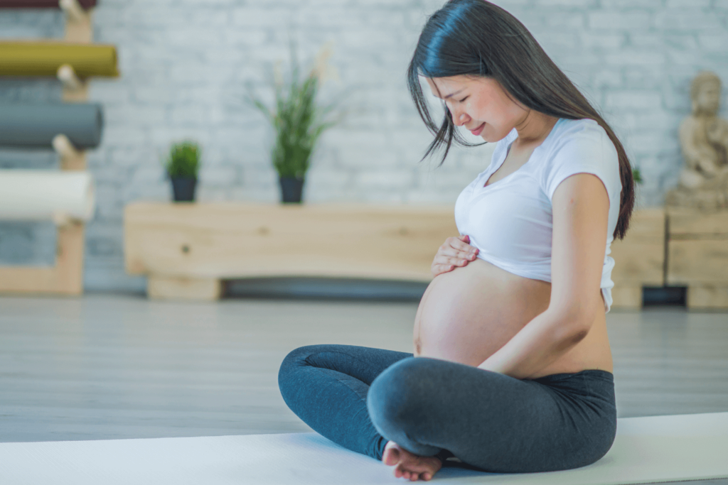 Pregnant woman sitting cross-legged on a yoga mat, cradling and looking at her stomach