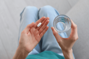 Woman holding a glass of water in one hand and a pill in the other hand