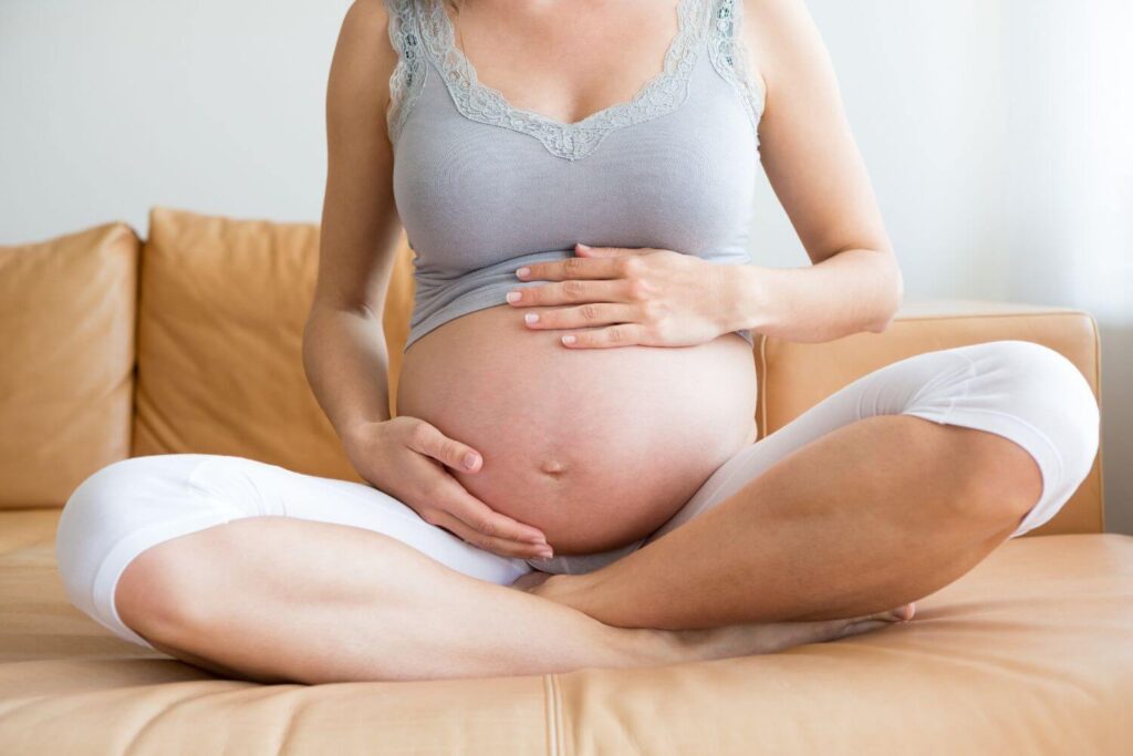 Pregnant woman is sitting on a couch holding her belly