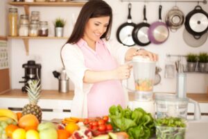 Pregnant woman in her kitchen blending fruits and vegetables