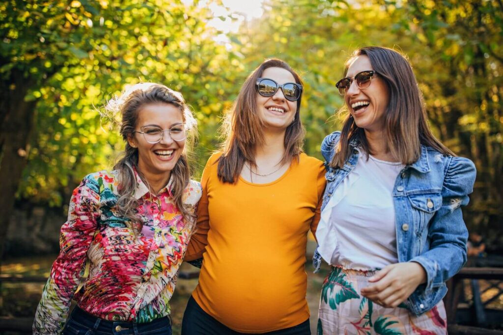 A pregnant woman locked arms and laughing with two of her friends