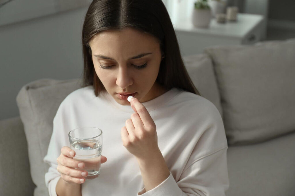Woman holding a glass of water and a white pill to her mouth