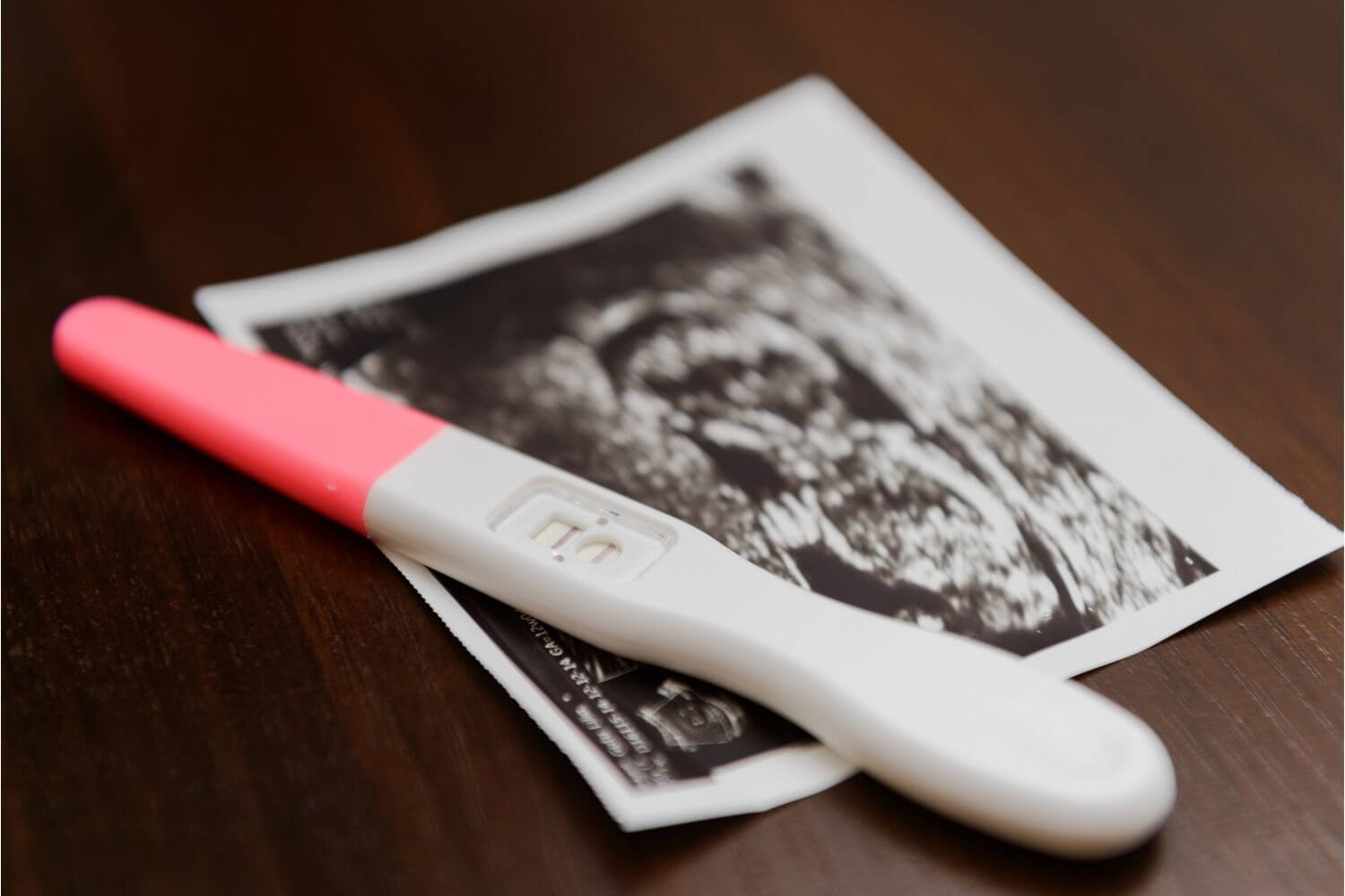Positive pregnancy test sits on top of an ultrasound image