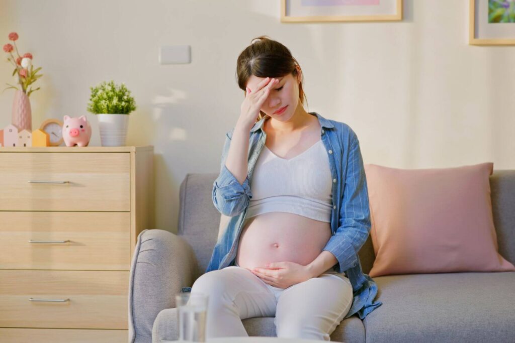 Pregnant woman sitting on a couch, holding her belly and her head