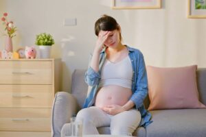 Pregnant woman sitting on a couch, holding her belly and her head