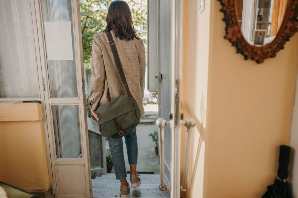 A woman is leaving her home with a bag on her shoulder