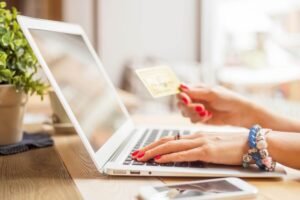 A woman is holding her credit card in one hand and placing an online order on her laptop