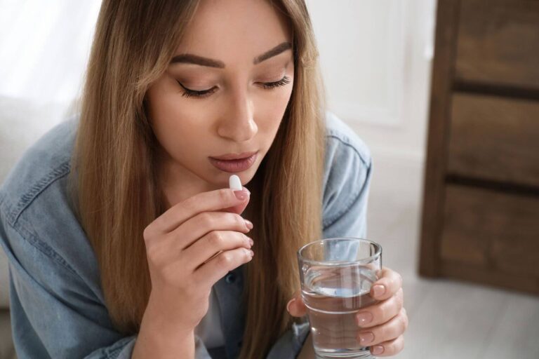 Woman holding a glass of water and a white pill