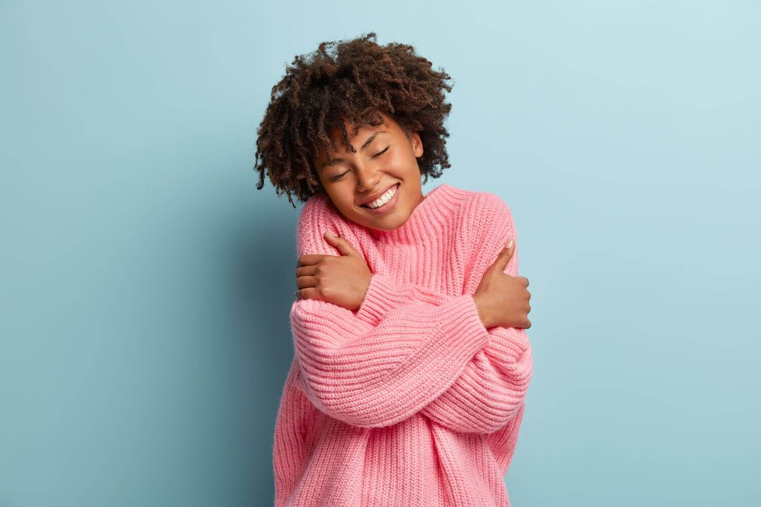Woman in a pink sweater smiling and hugging herself