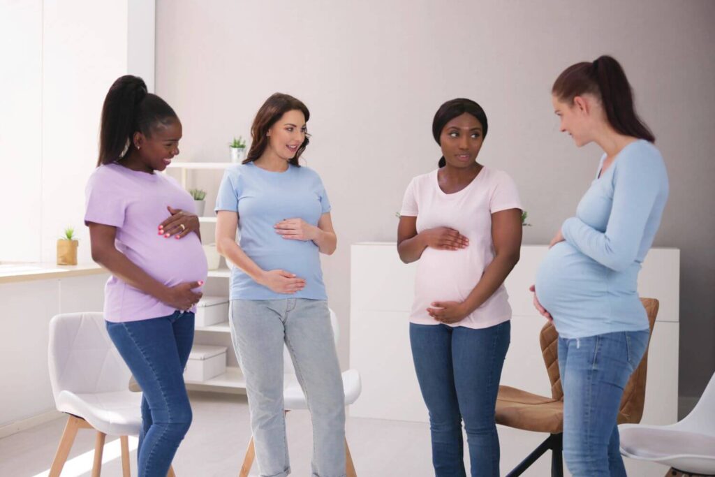 Four pregnant women standing together, embracing their bellies