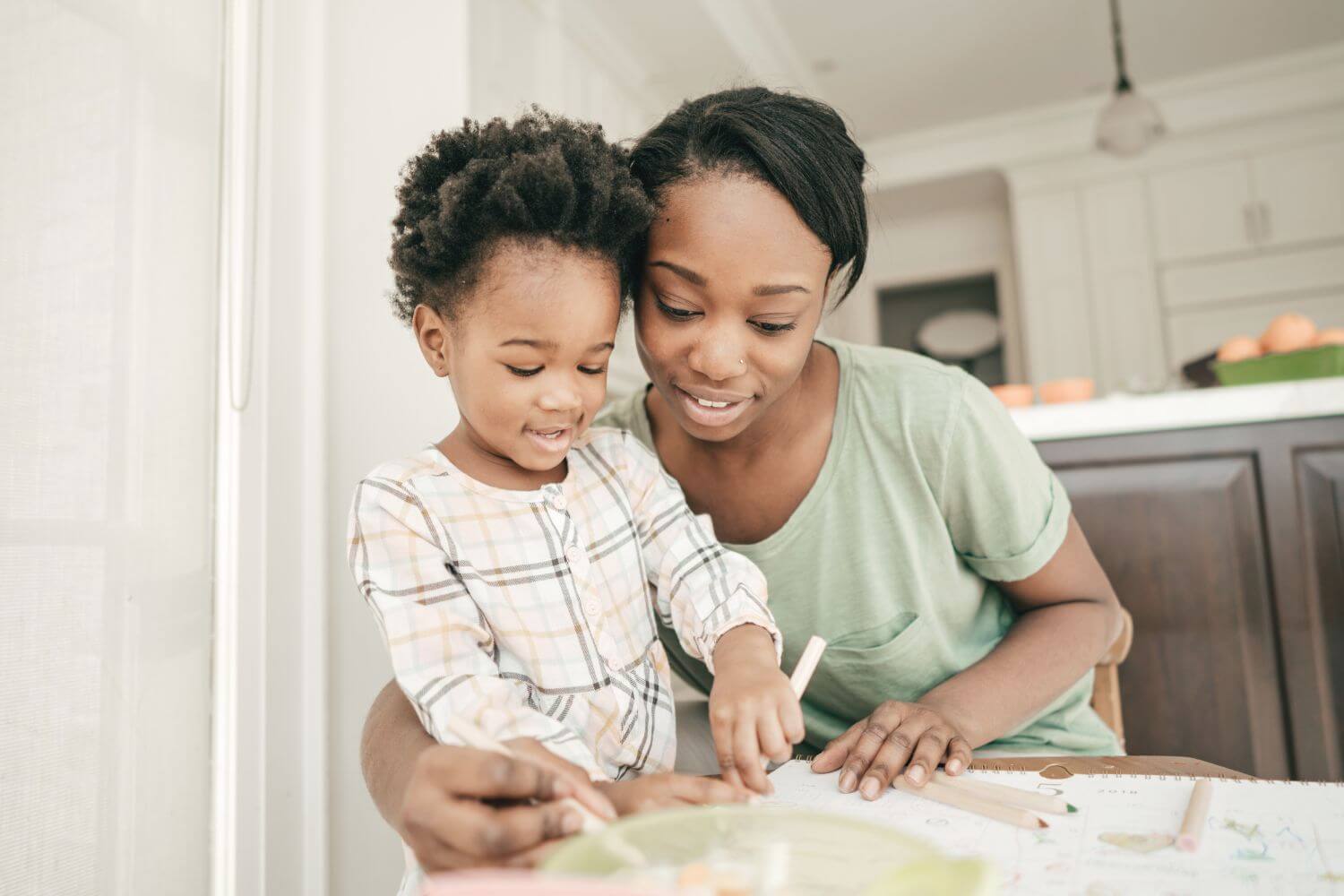 A mother embracing her toddler child while doing crafts at a table