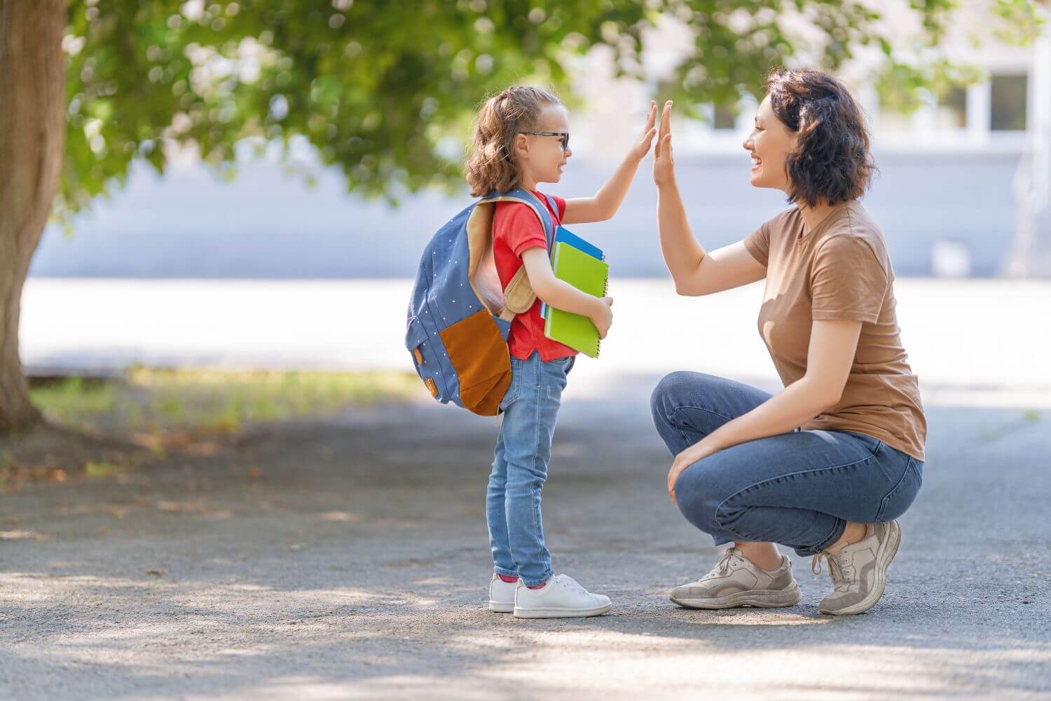 mother high fiving her daughter who is wearing a backpack and holding folders