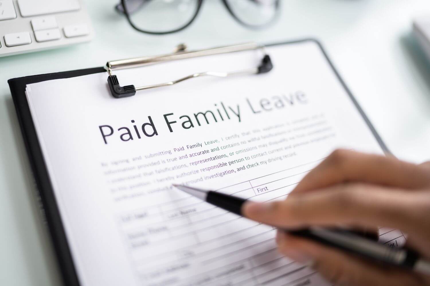 a black clipboard holds FMLA documents with a hand hovering over the paper