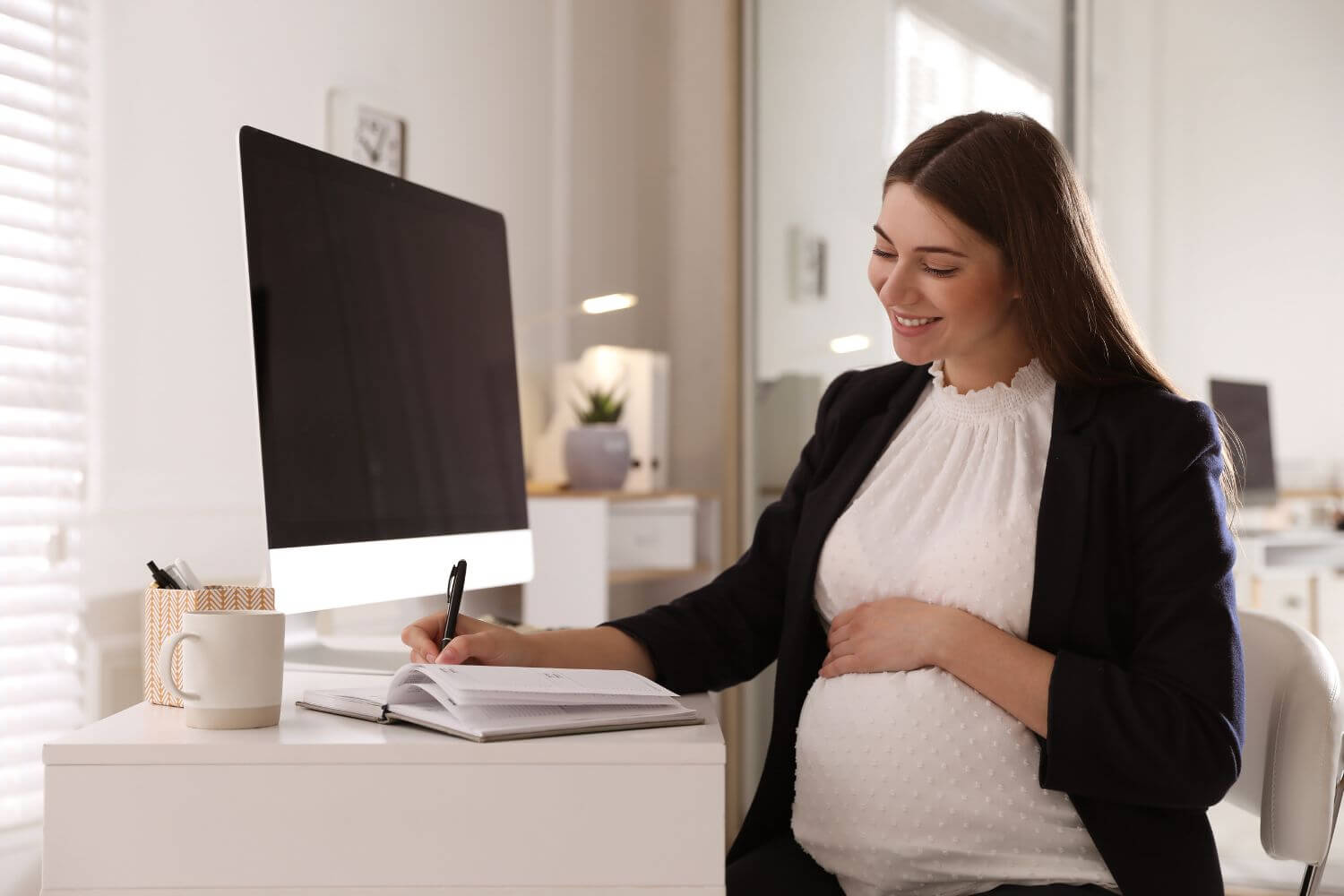 pregnant woman sitting at a desk writing in a notebook