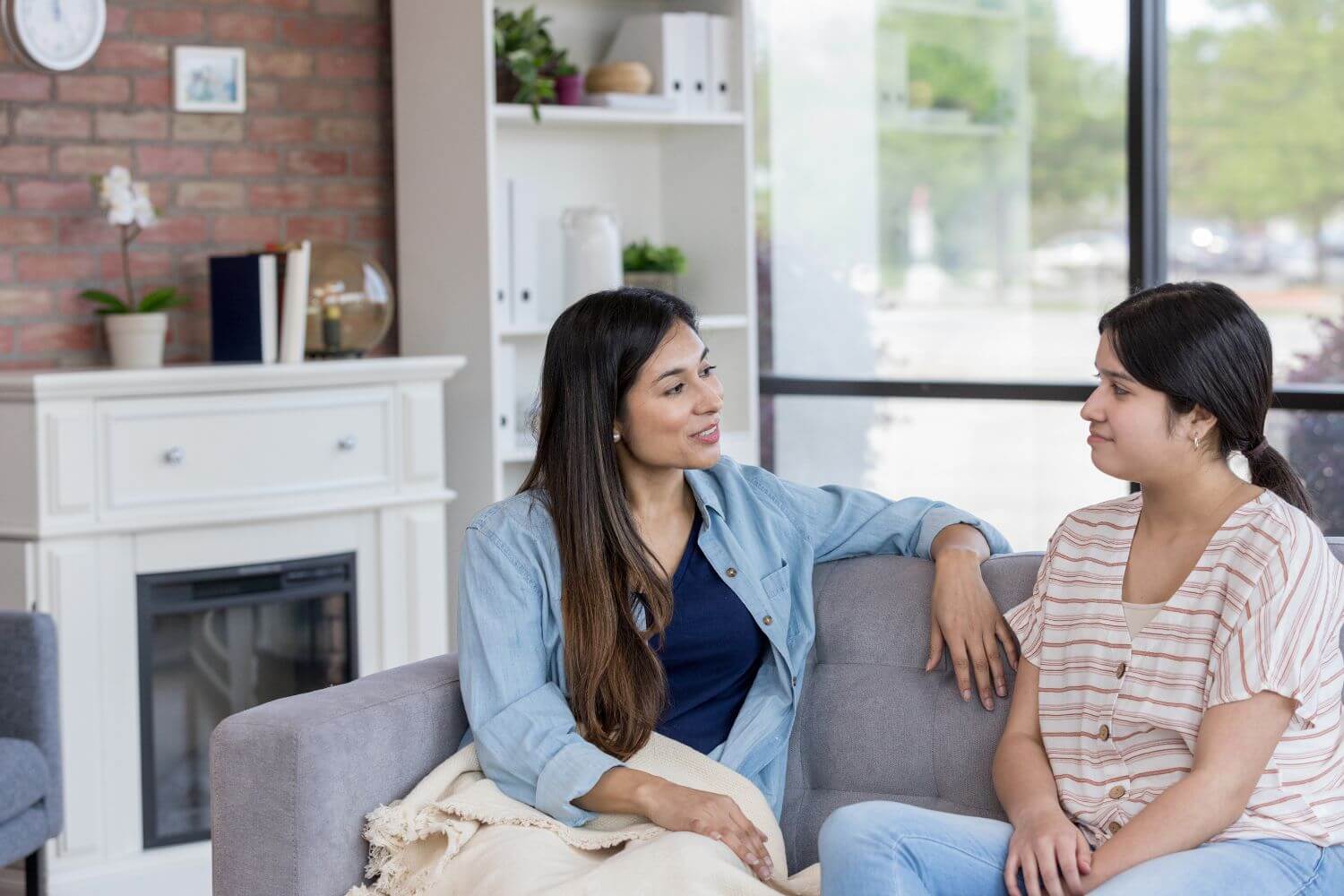 Teenage girl sits on a couch next to her mother while they are in discussion