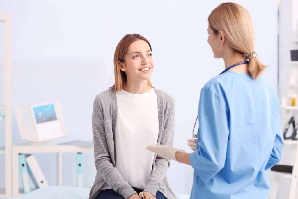 A woman sitting on a table is in conversation with her healthcare provider