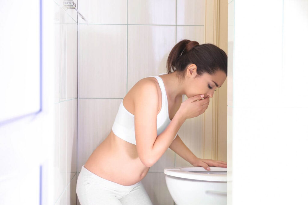 Woman leaning over a toilet as she holds her hand to her mouth due to nausea