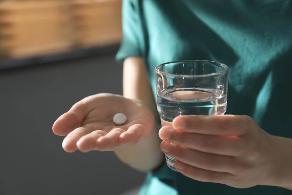 woman in a green shirt holding a glass of water and a white pill