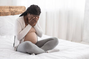 Pregnant woman struggling with depression holds her head in her hands