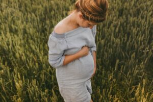 A pregnant woman wearing a blue dress poses in a field of grass