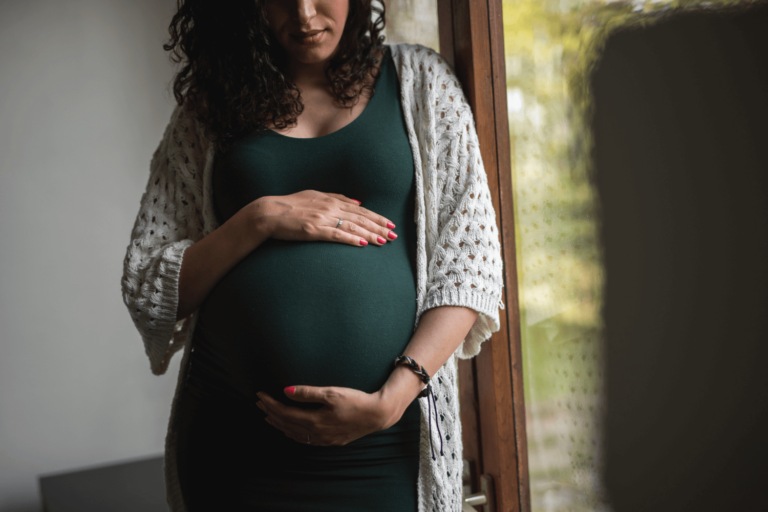 Pregnant woman looking down at and holding her belly with both hands