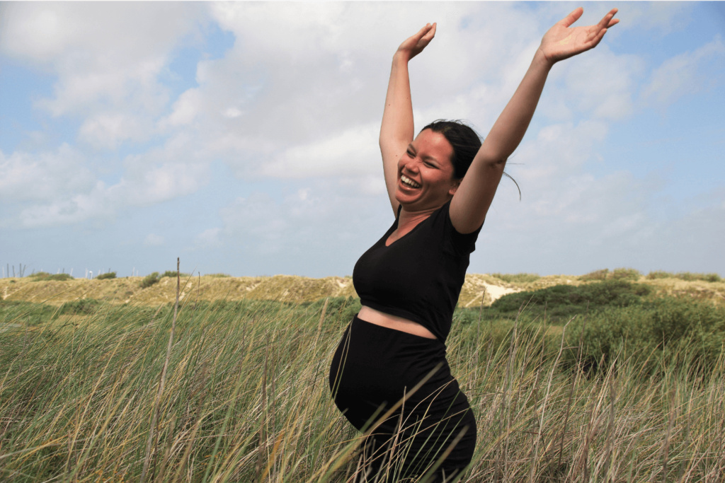 Joyful pregnant woman wearing all black is frolicking in a field with her hands in the air