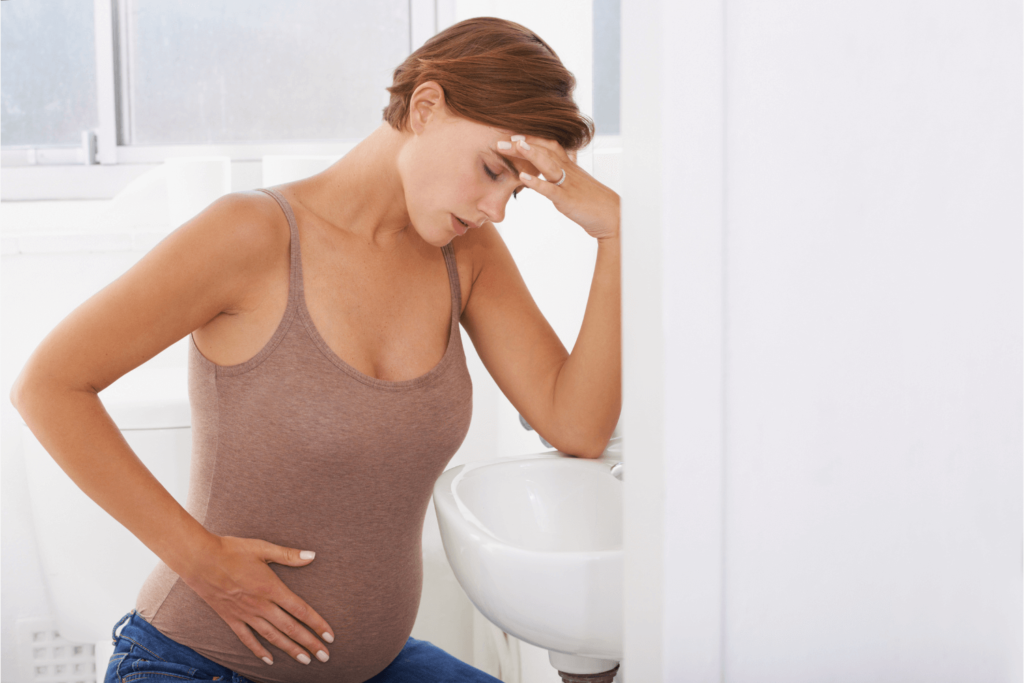 Nauseous pregnant woman kneeling over, holding her head and her stomach