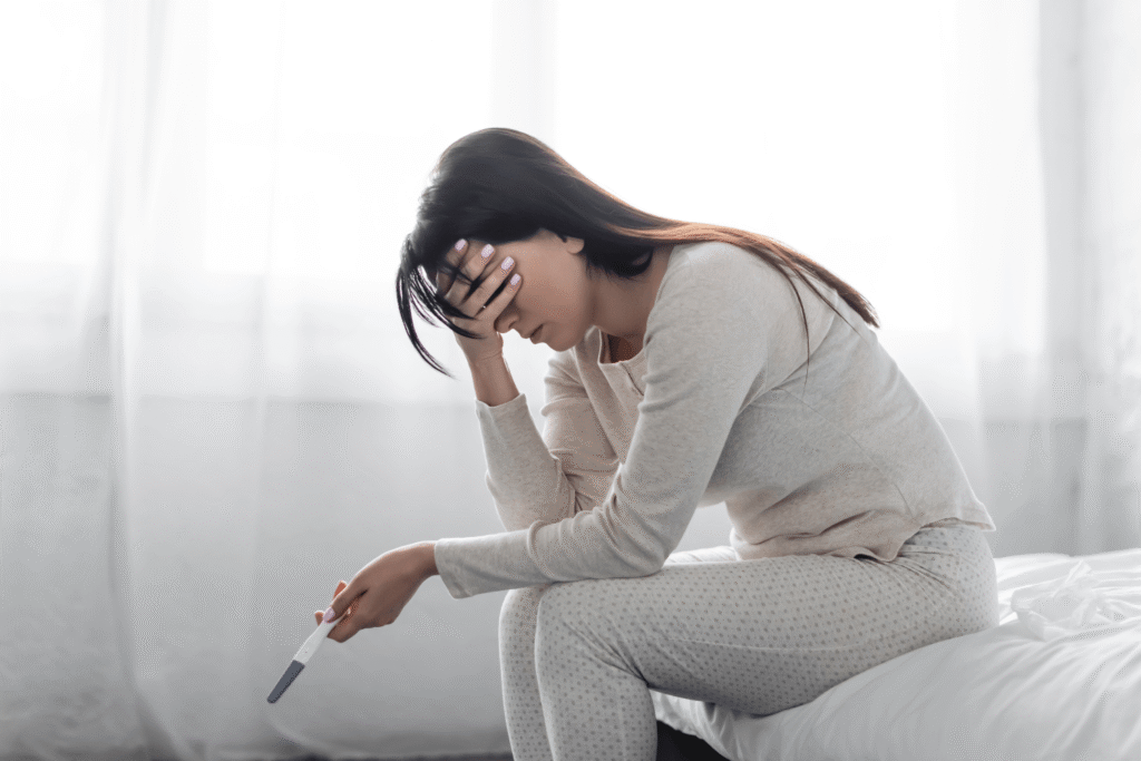 woman in pajamas holding her head and a pregnancy test