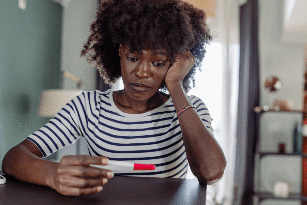 woman staring at a pregnancy test while holding her head