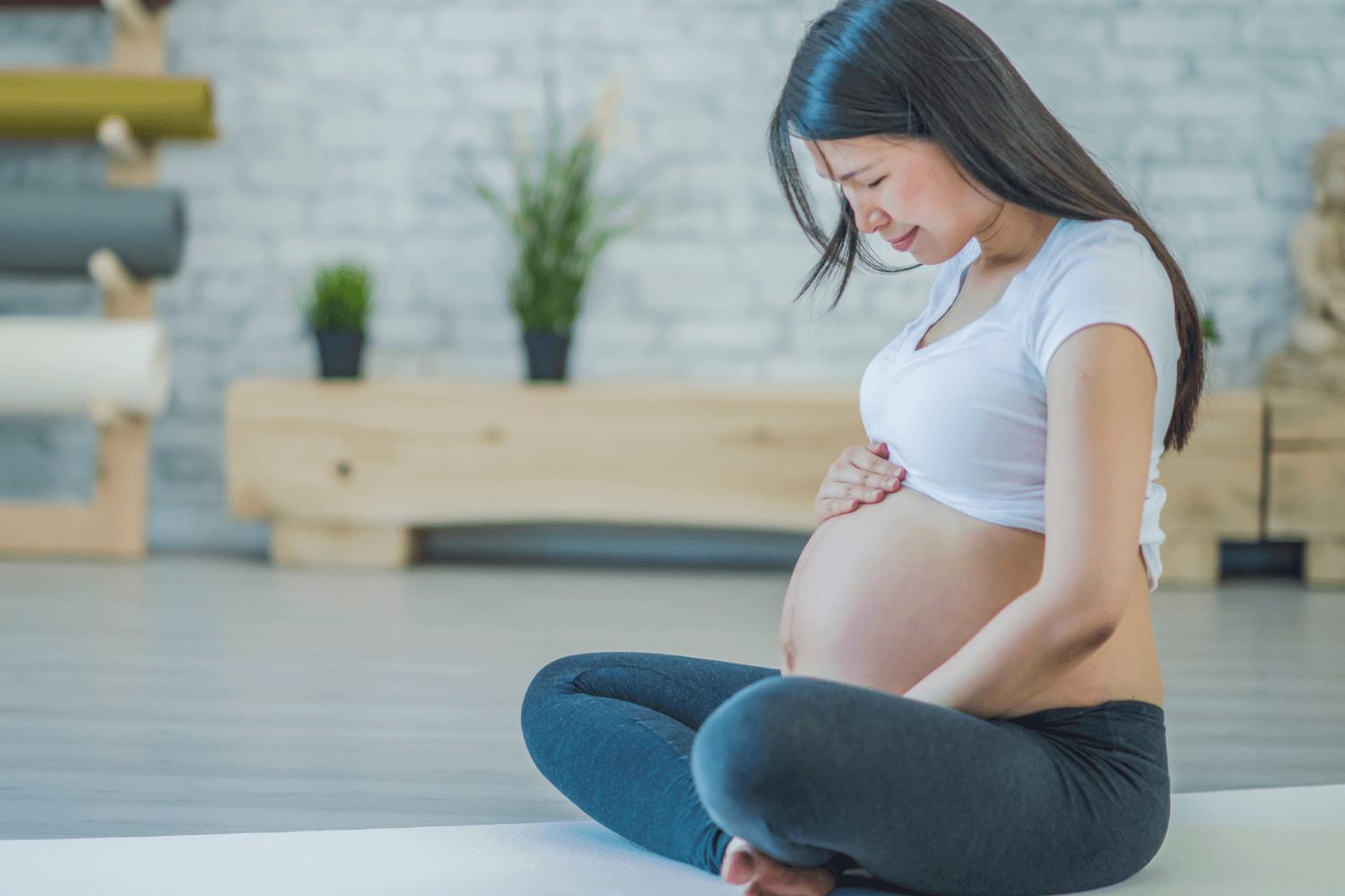 pregnant woman sitting on a yoga mat while holding her belly