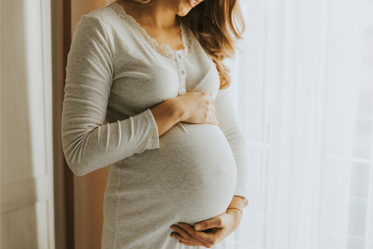 Pregnant woman in a nightgown embracing her belly