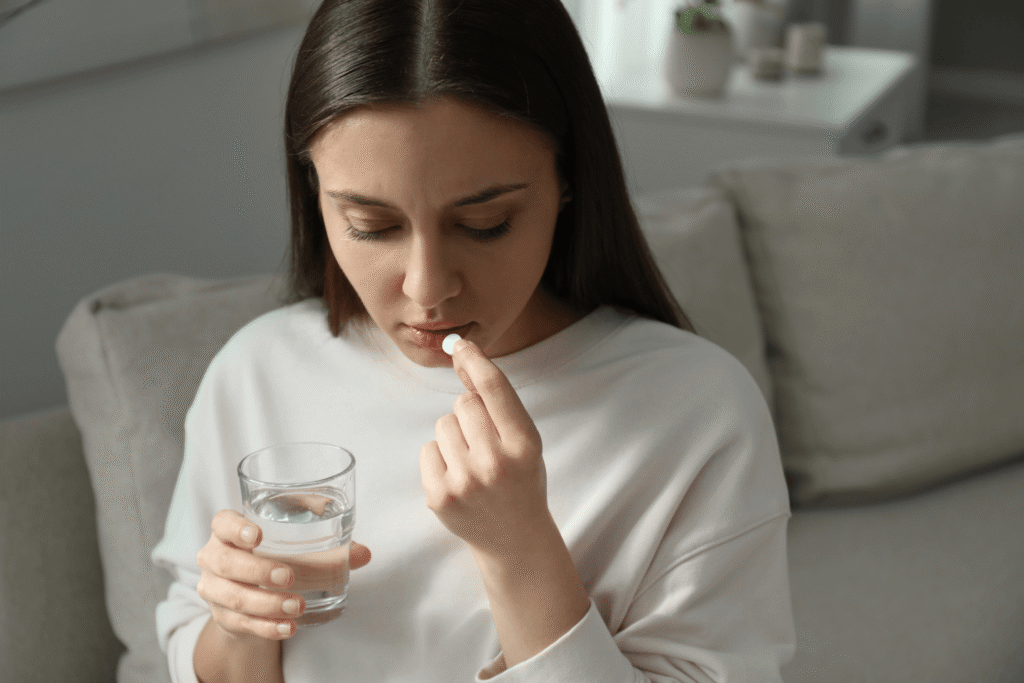 Woman holding a glass of water and a white pill to her mouth