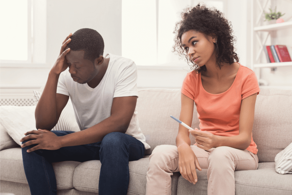 Woman holding a pregnancy test looking at her unsupportive partner who is stressed