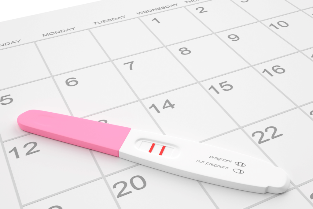 A positive pregnancy test sitting on top of a desk calendar