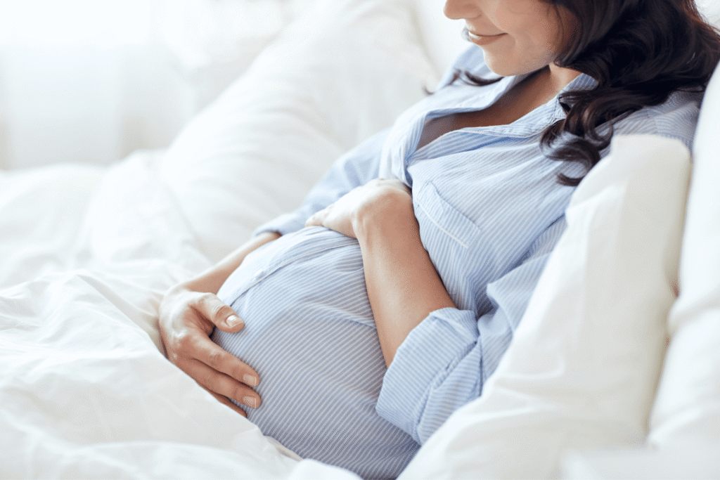 pregnant woman laying in bed holding her belly