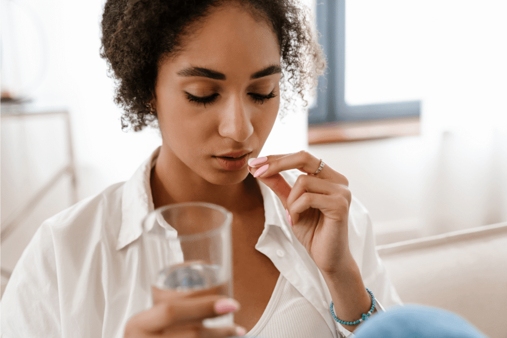 Woman holding a glass of water and a white pill near her mouth