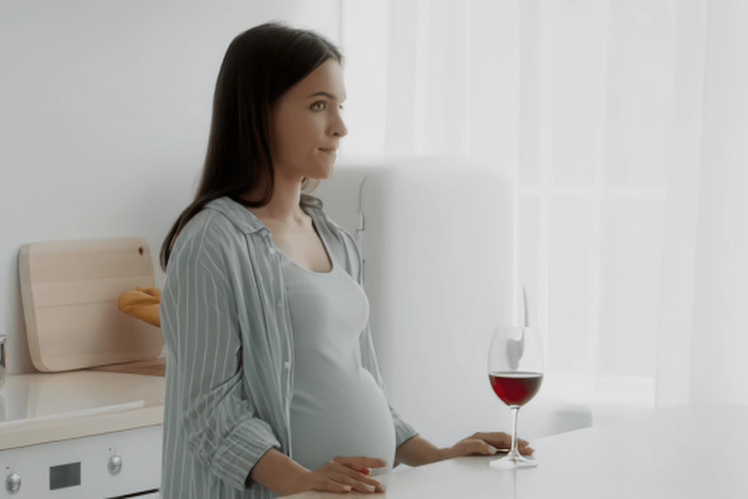 pregnant woman standing at a table with a glass of wine