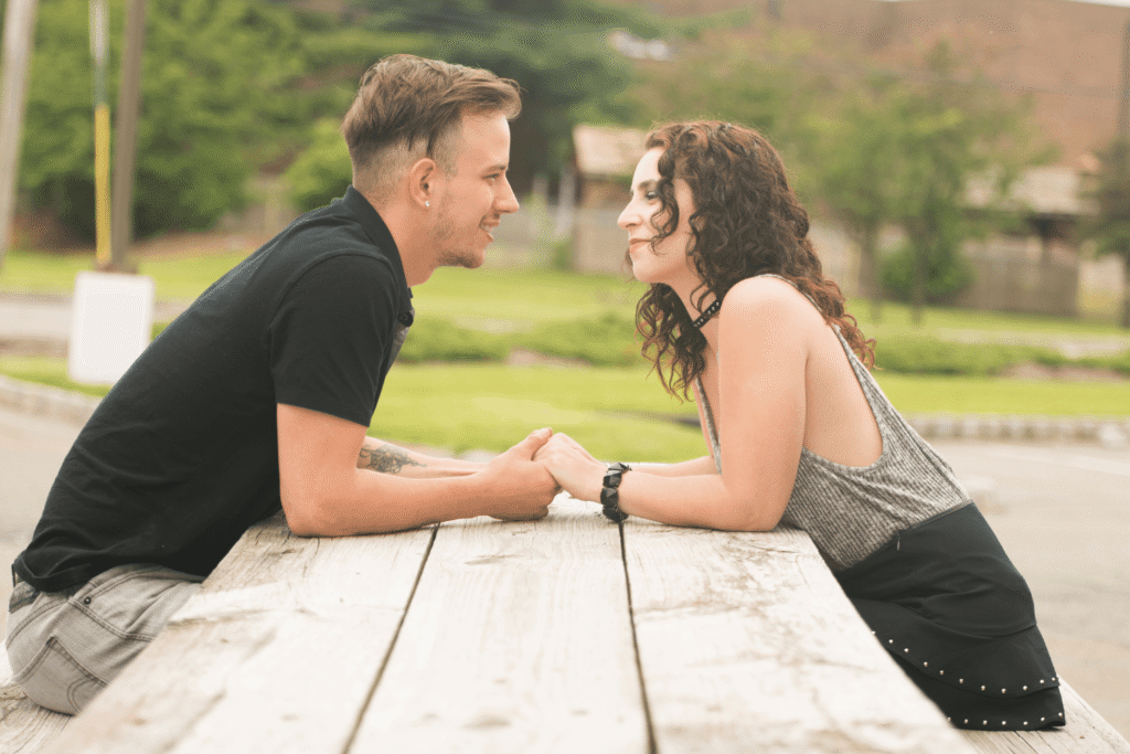 A young couple sitting across from one another on a picnic bench while holding hands