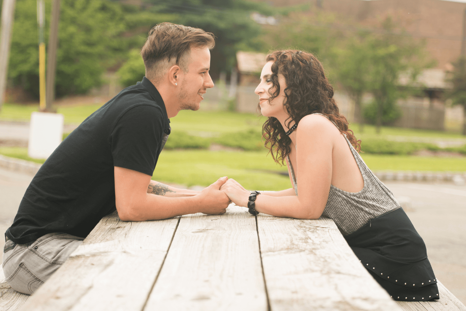 A young couple sitting across from one another on a picnic bench while holding hands