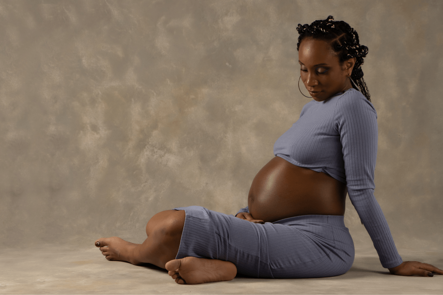 Pregnant woman in a gray matching set is sitting on the floor