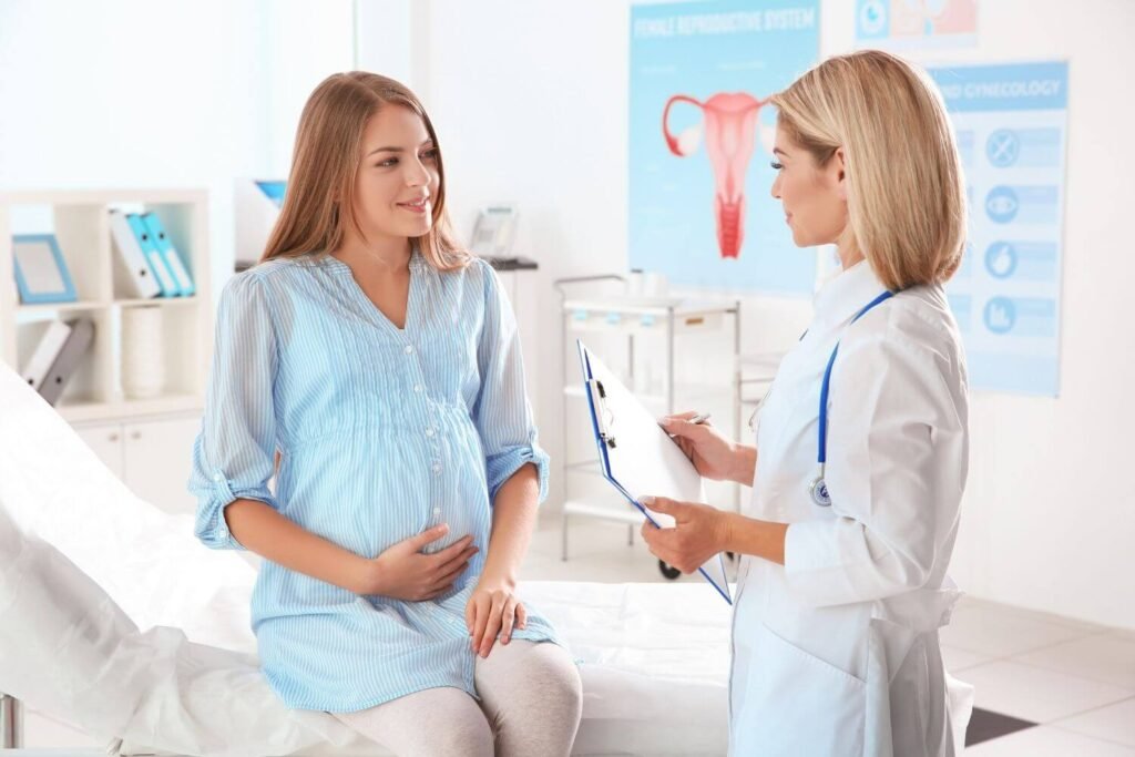 Pregnant woman sitting on an exam table speaking with her OBGYN